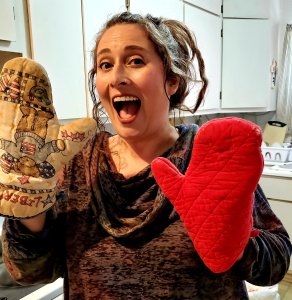 Dawn Michelle Michals hold her hands up with a red oven mitt on her left hand and a teddy bear oven mitt on her right. She is extremely happy and smiling with her mouth open. 